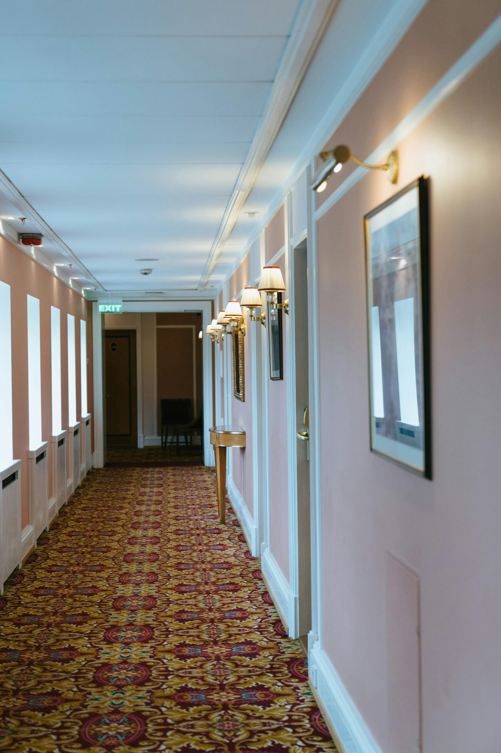 Hotel hallway with pink walls and patterned carpet. 