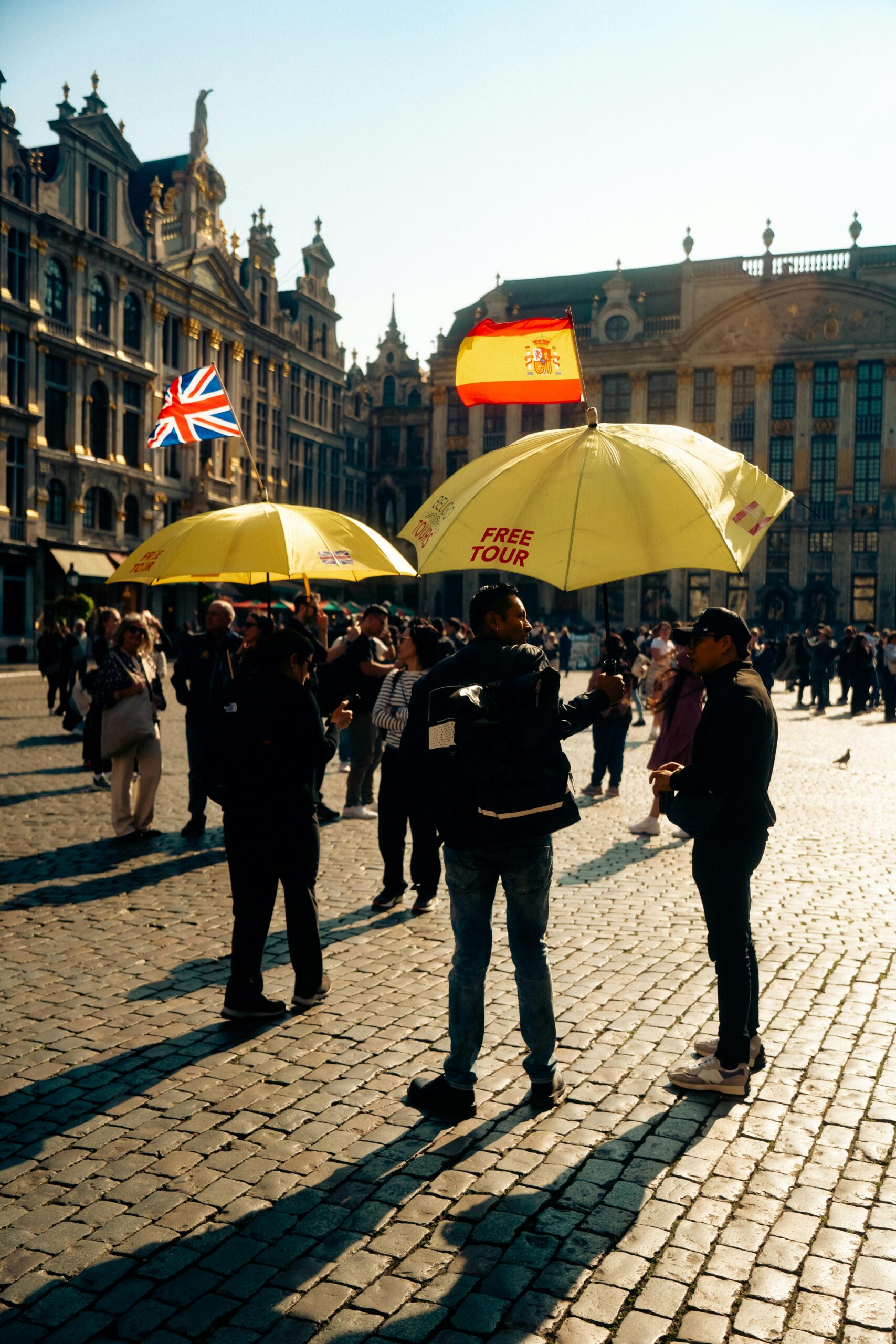 Group of people standing on a cobblestone street, two holding yellow umbrellas advertising free tours.