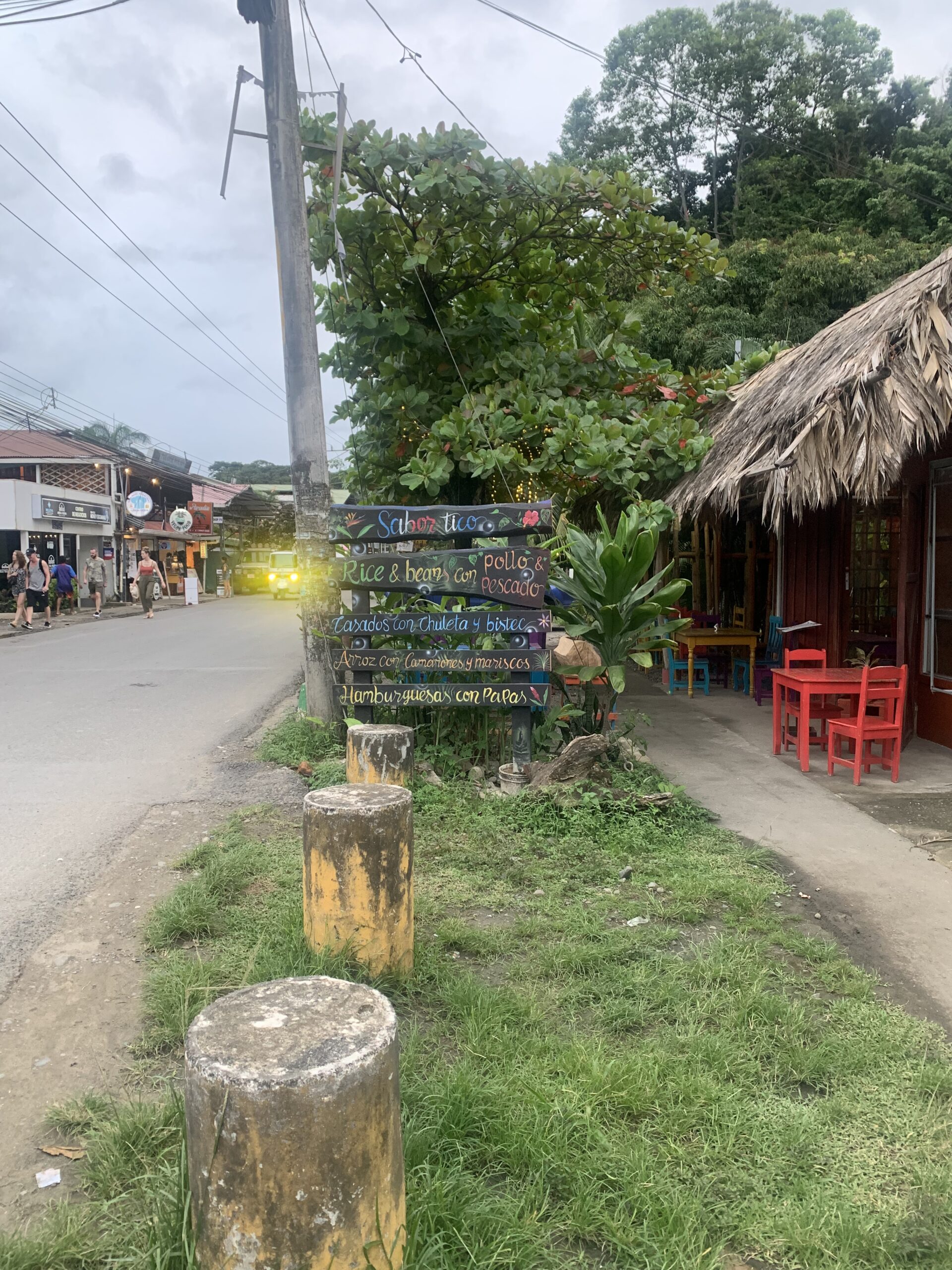 Street view in Puerto Viejo Costa Rica, advertisement of restaurant menu and tourists across the street walking.
