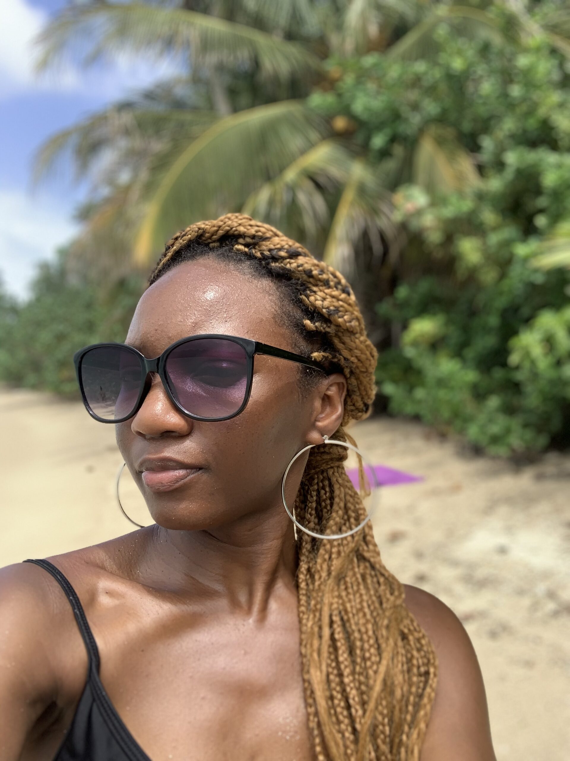 Woman in sunglasses on a beach with green trees in the background